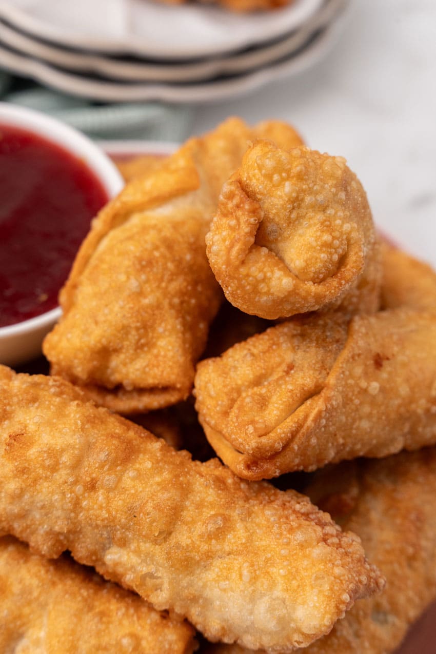 leftover thanksgiving egg rolls stacked on a dinner plate with a small white bowl of cranberry sauce on the side