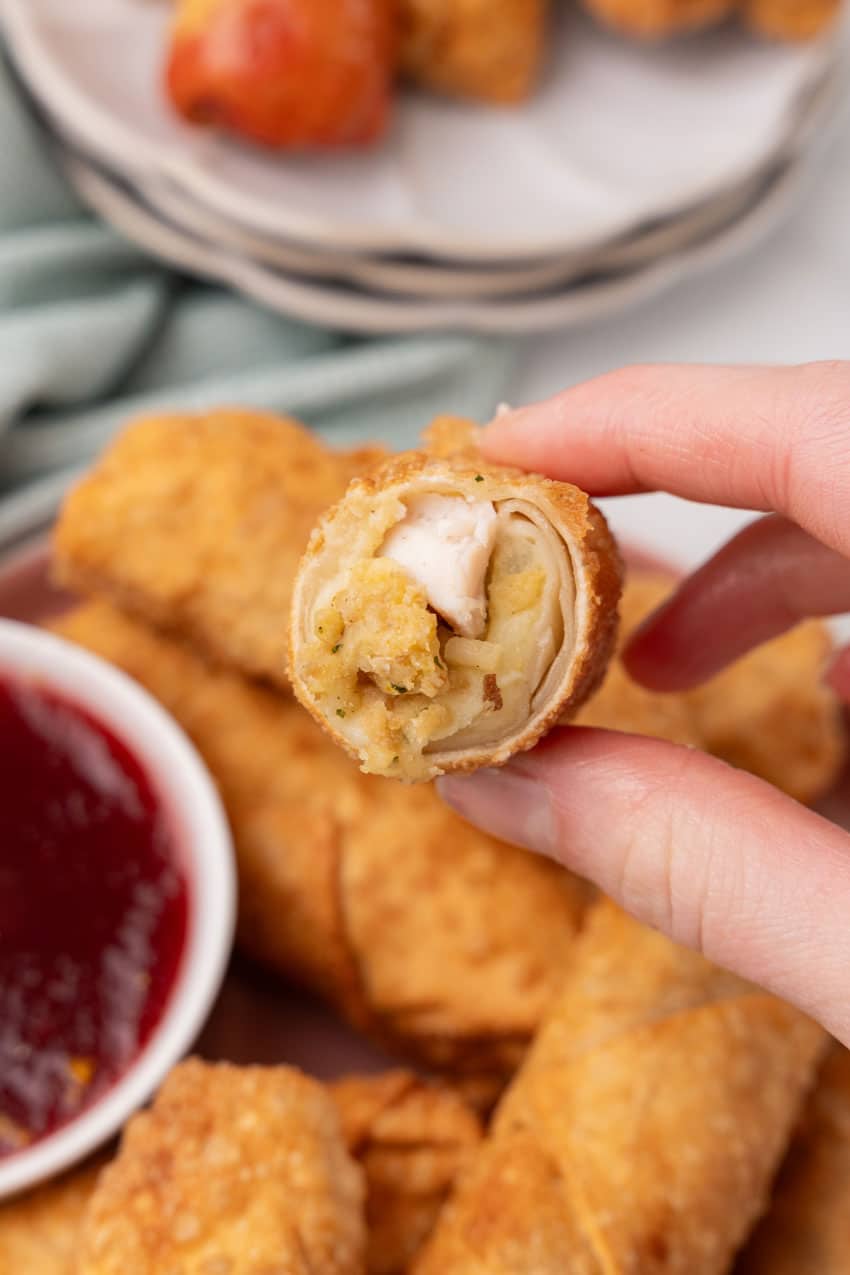 a hand holding up half of a thanksgiving egg roll showing the filling inside