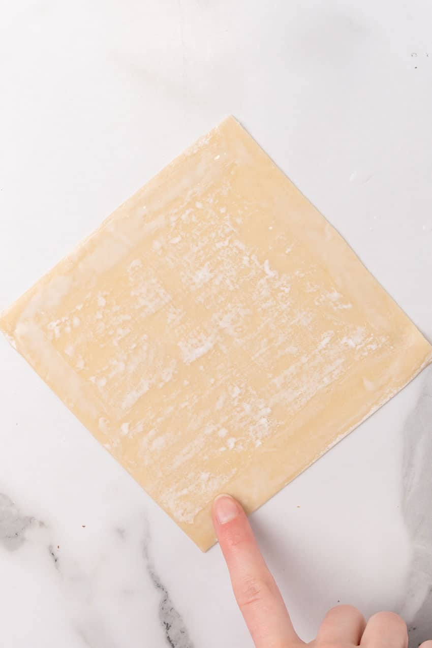 a finger rubbing a mixture of cornstarch and water along the inside edges of an egg roll wrapper