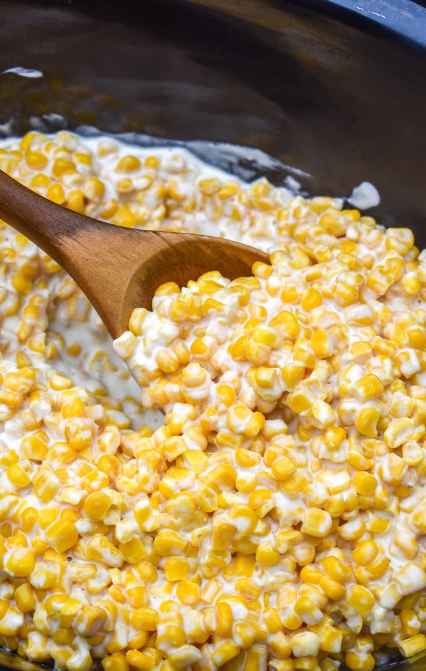 a wooden spoon resting in a black crock filled with slow cooker creamed corn