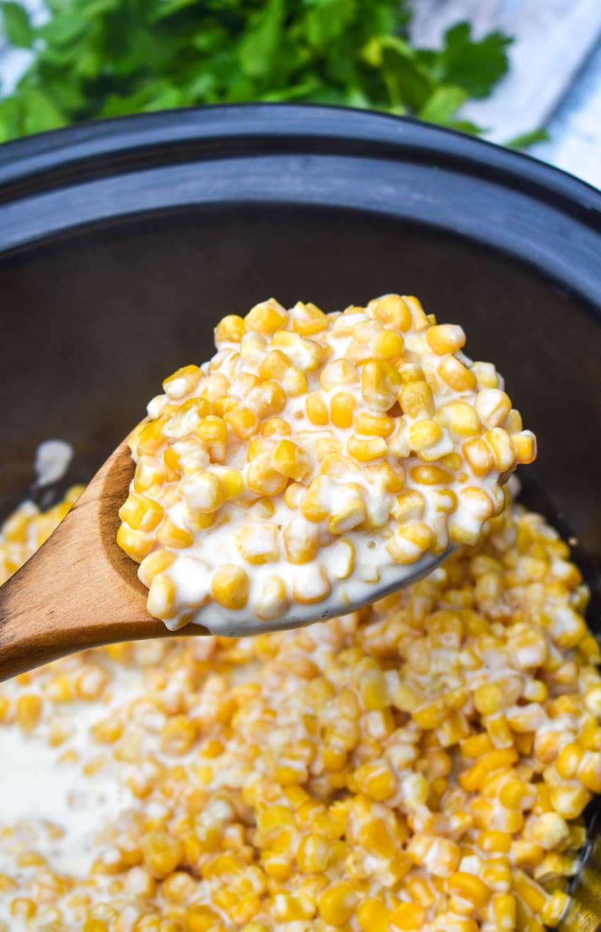 a wooden spoon holding up a scoop of slow cooker creamed corn