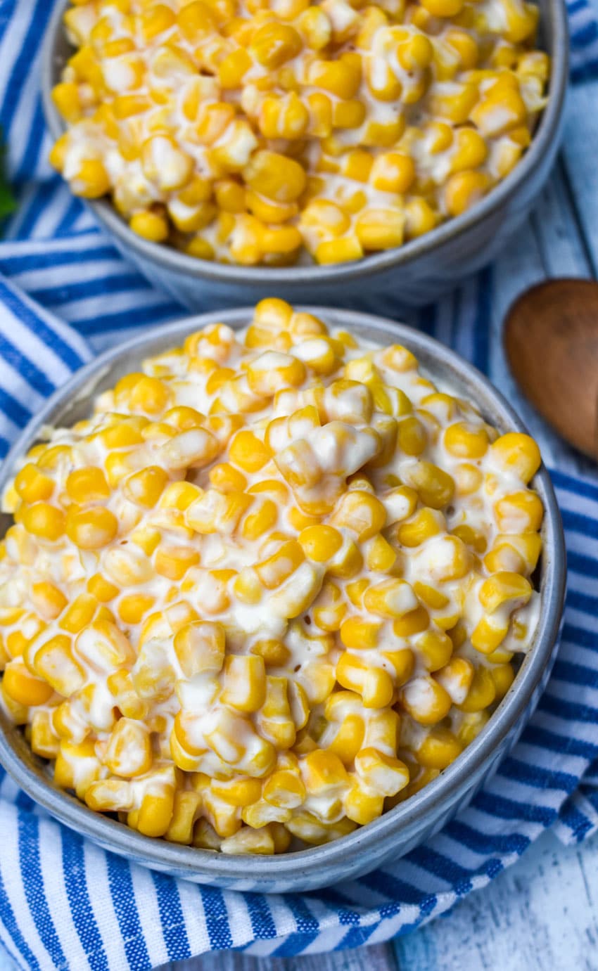 slow cooker cream corn in two small gray bowls with wooden spoons on the side