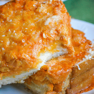 two slices of tomato soup dipped grilled cheese stacked on a white plate