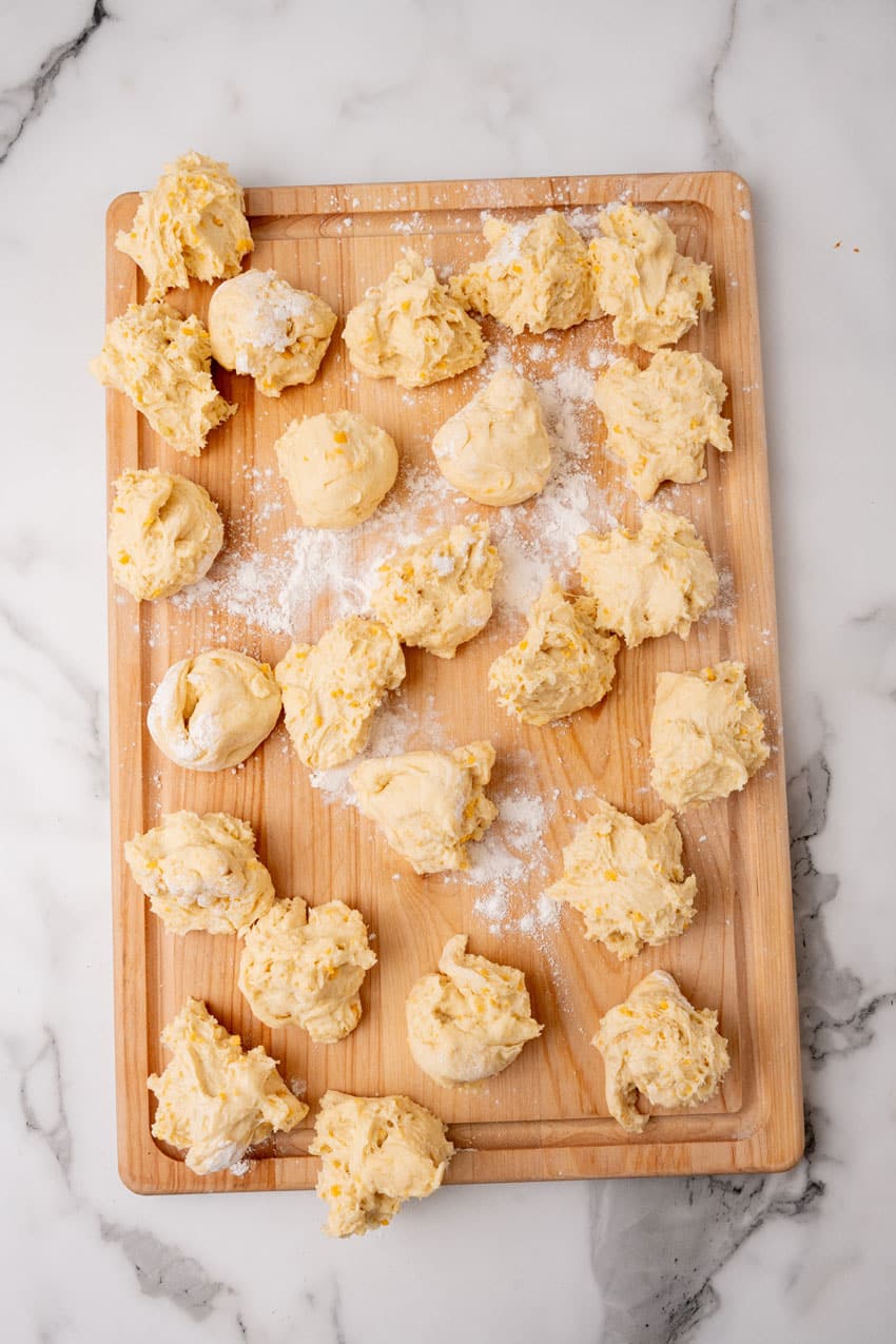 balls of cheesy potato roll dough on a floured wooden cutting board