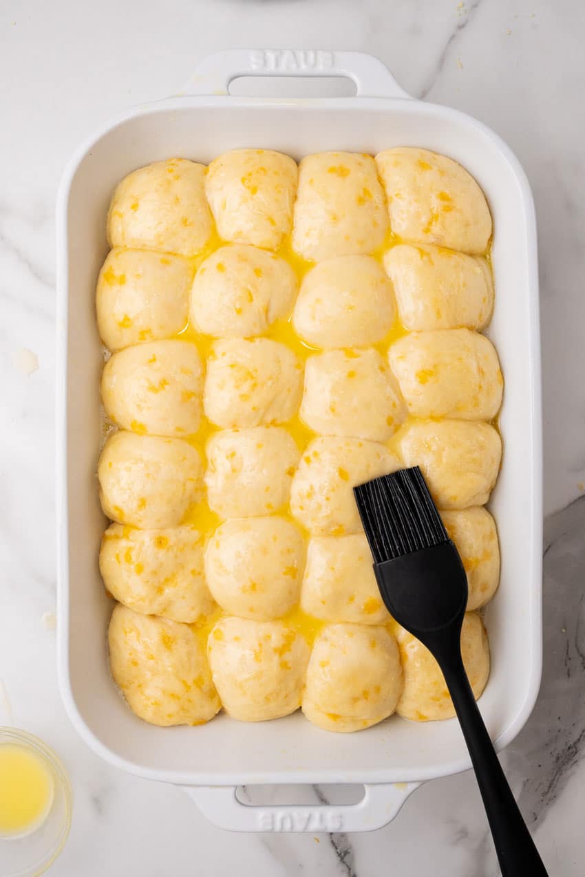 buttered balls of cheesy potato roll dough arranged in rows in a white casserole dish