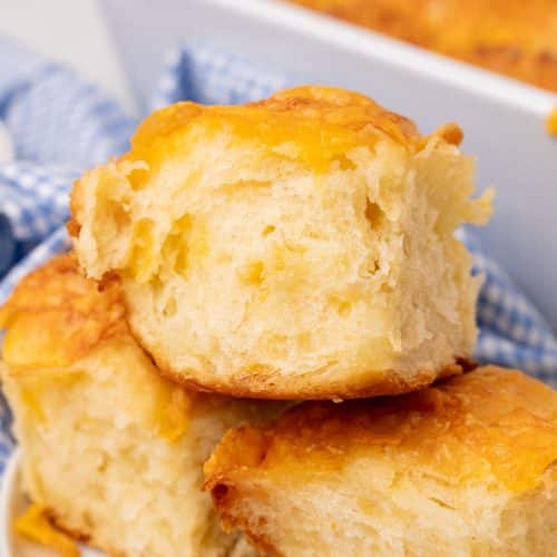 three cheesy pull apart potato rolls stacked on a small white plate