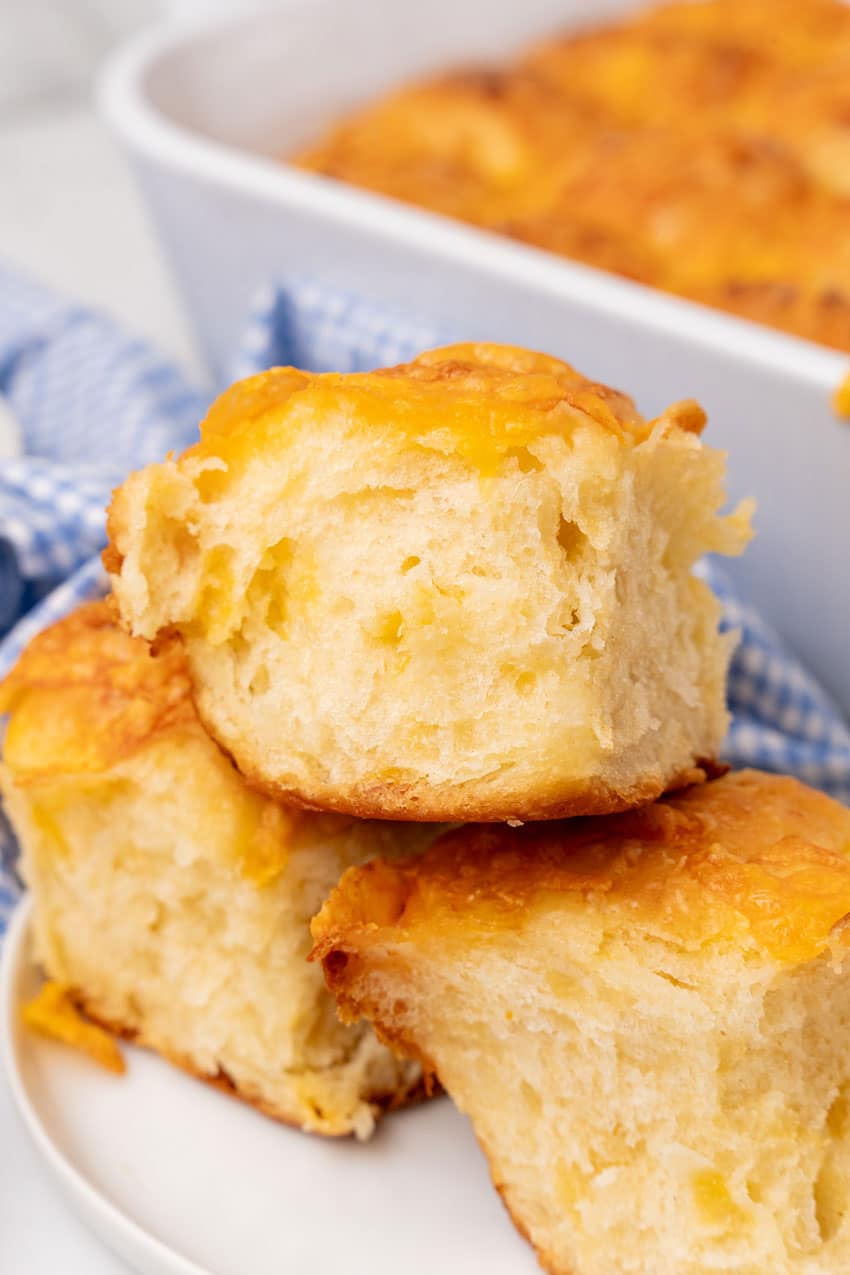 three cheesy pull apart potato rolls stacked on a small white plate