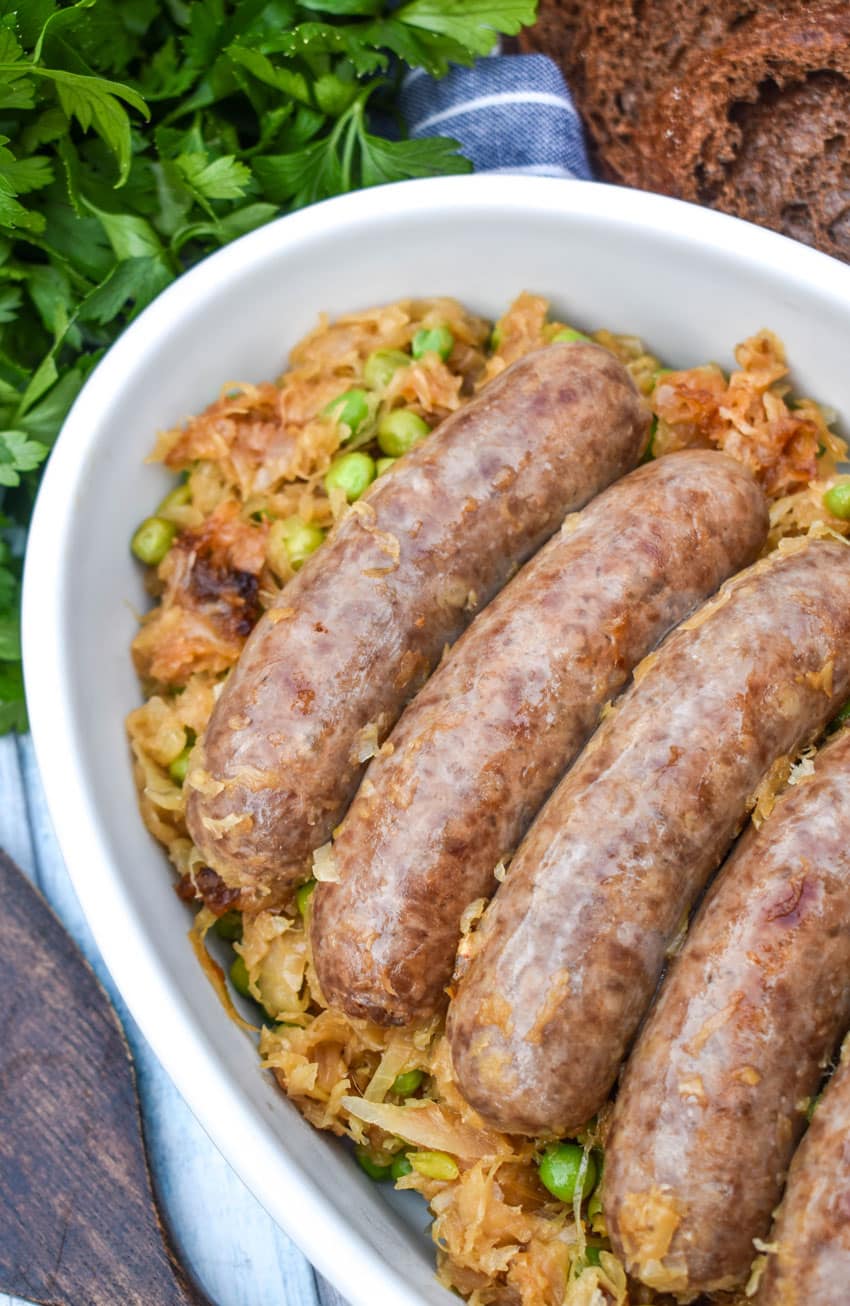 COOKED BEER BRATWURST RESTING ON A BED OF CARAMELIZED SAUERKRAUT IN A WHITE SERVING DISH