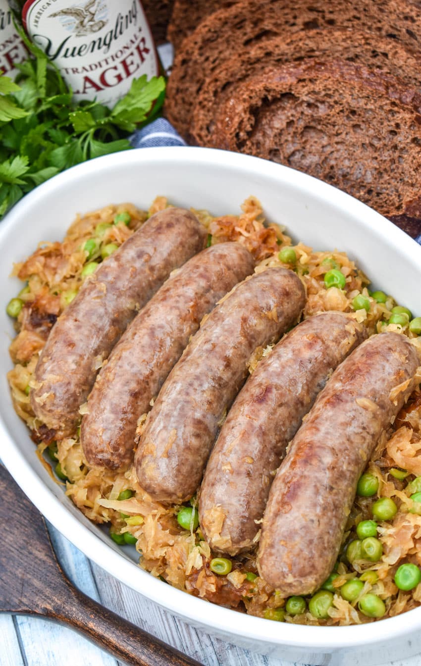 COOKED BEER BRATWURST RESTING ON A BED OF CARAMELIZED SAUERKRAUT IN A WHITE SERVING DISH