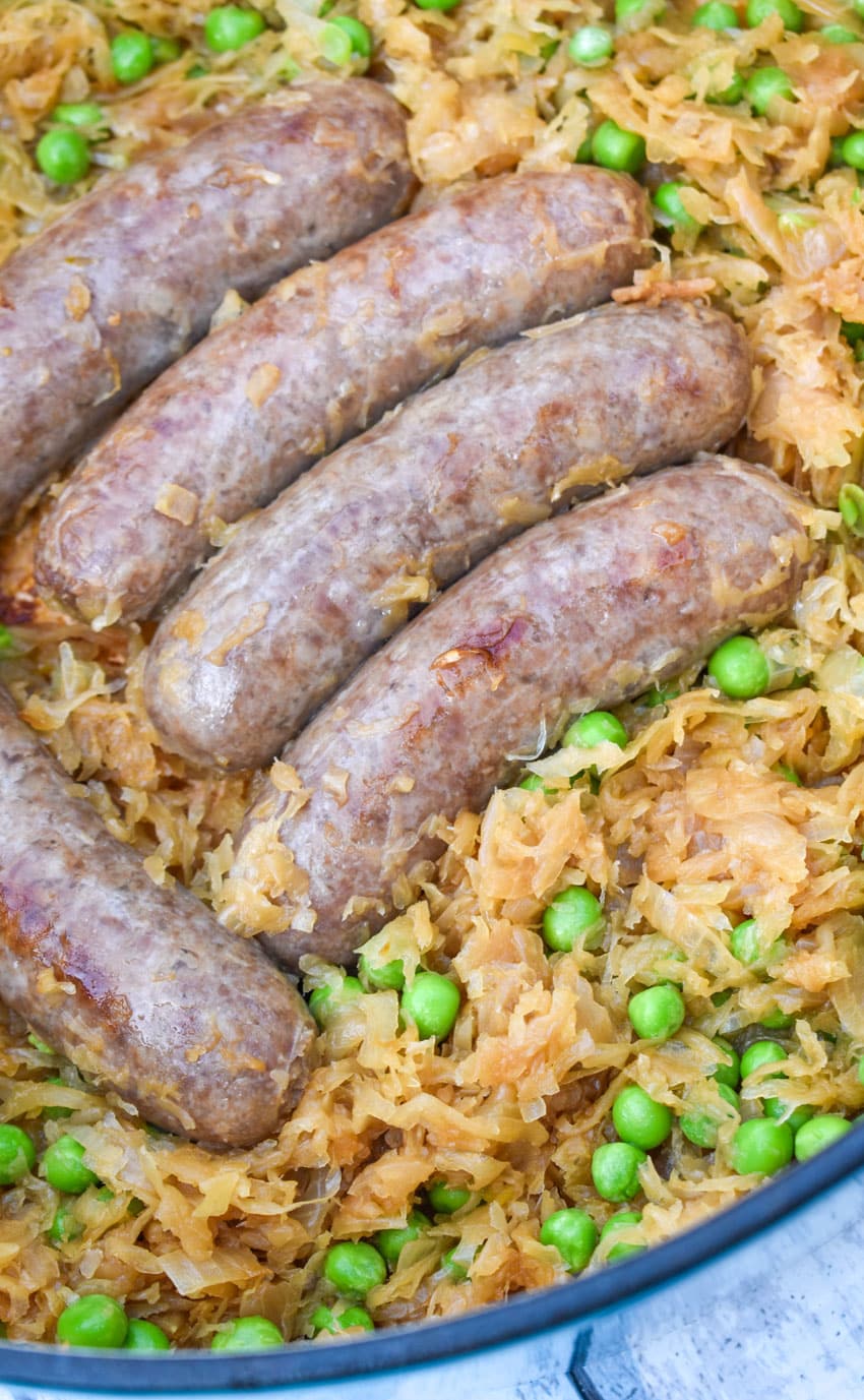 A CLOSE UP OF COOKED BEER BRATWURST RESTING ON A BED OF CARAMELIZED SAUERKRAUT IN A CAST IRON DUTCH OVEN