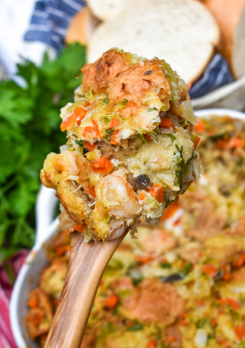 a wooden spoon holding up a scoop of baked seafood stuffing