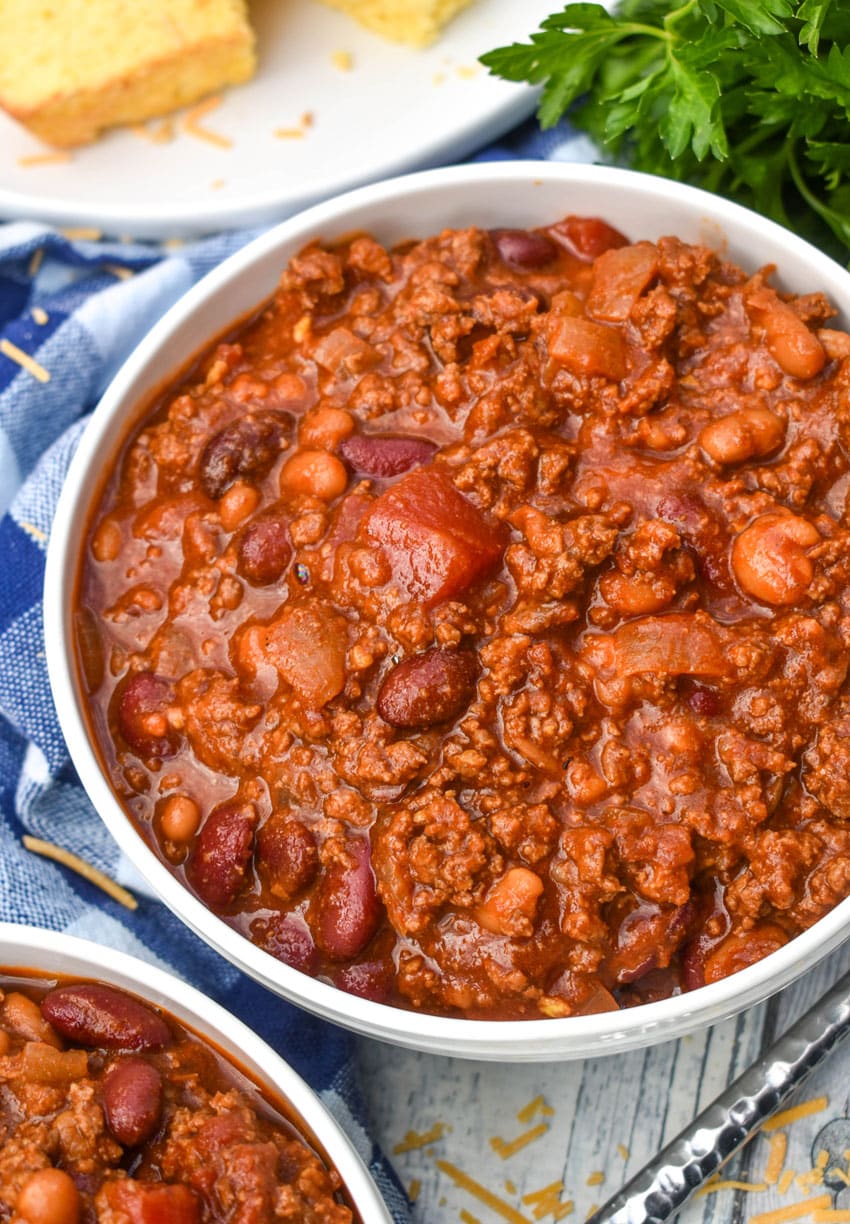 sweet and spicy chili in two white bowls with a plate of cornbread in the background