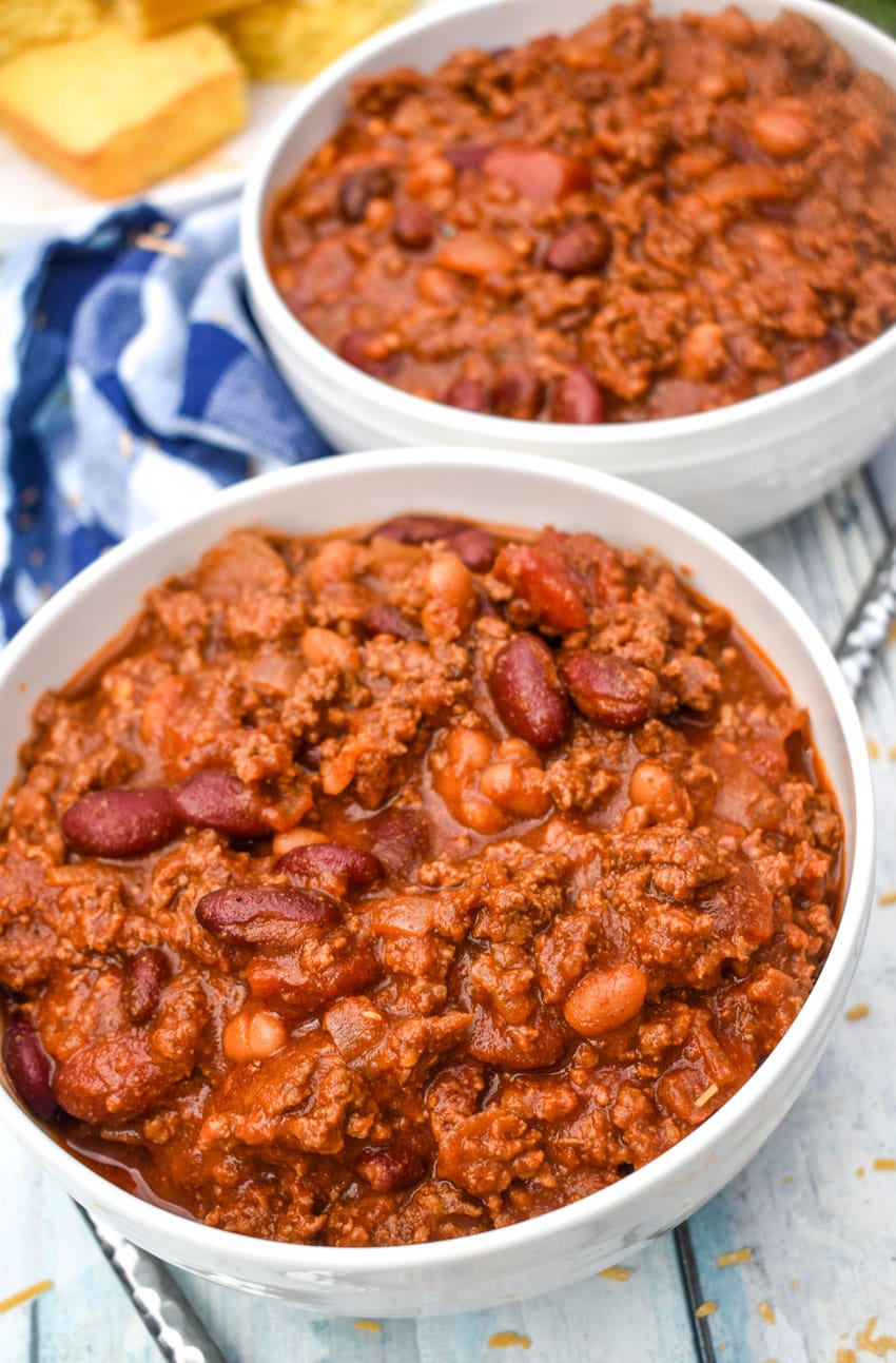 sweet and spicy chili in two white bowls with a plate of cornbread in the background
