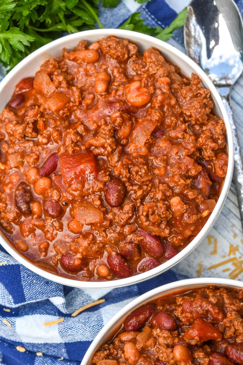 sweet and spicy chili in two white bowls with a plate of cornbread in the background