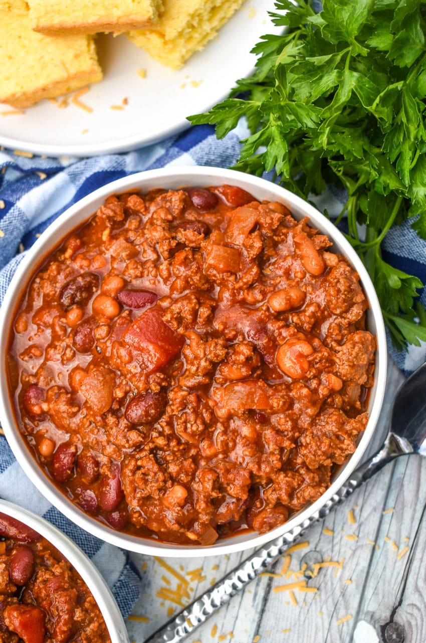 sweet and spicy chili in two white bowls with a plate of cornbread in the background