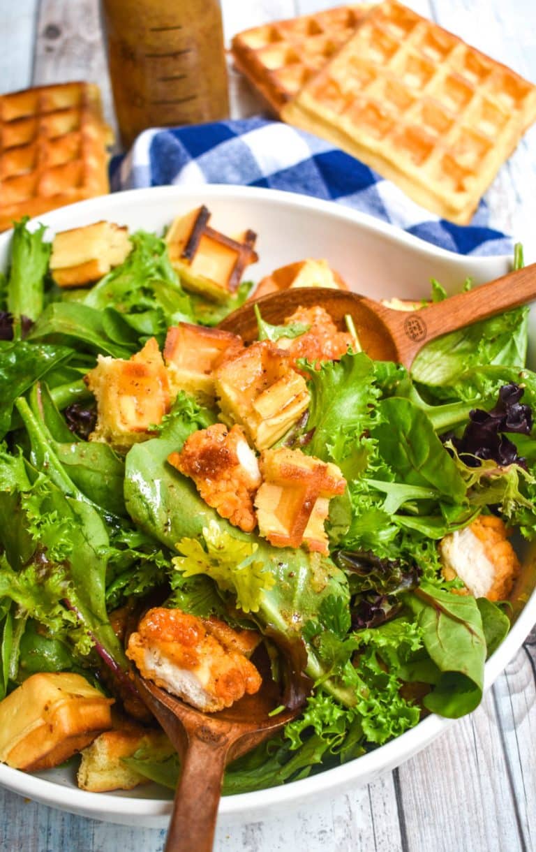 chicken and waffle salad in a white serving bowl with two wooden spoons resting on the sides