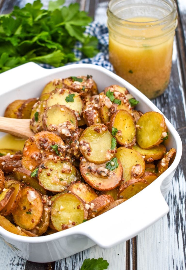 warm german potato salad in a white bowl with a wooden spoon