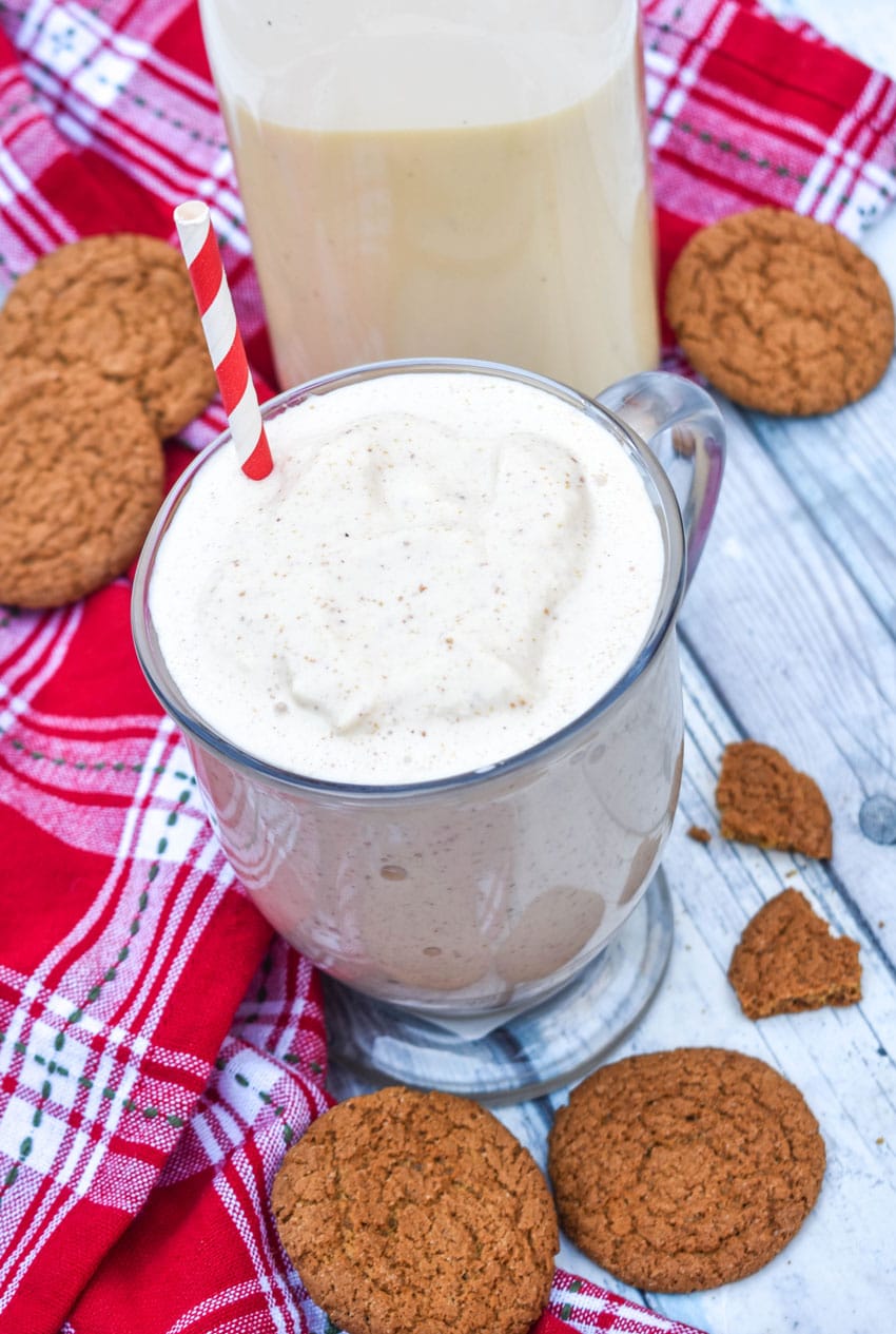 a gingerbread milkshake in a glass mug with a red and whipped striped straw sticking out