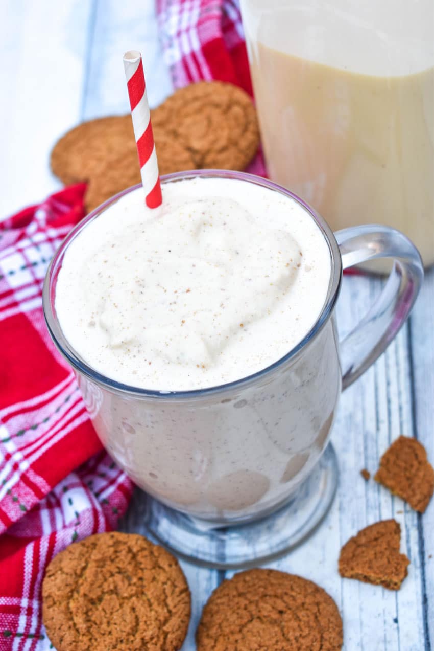 a gingerbread milkshake in a glass mug with a red and whipped striped straw sticking out