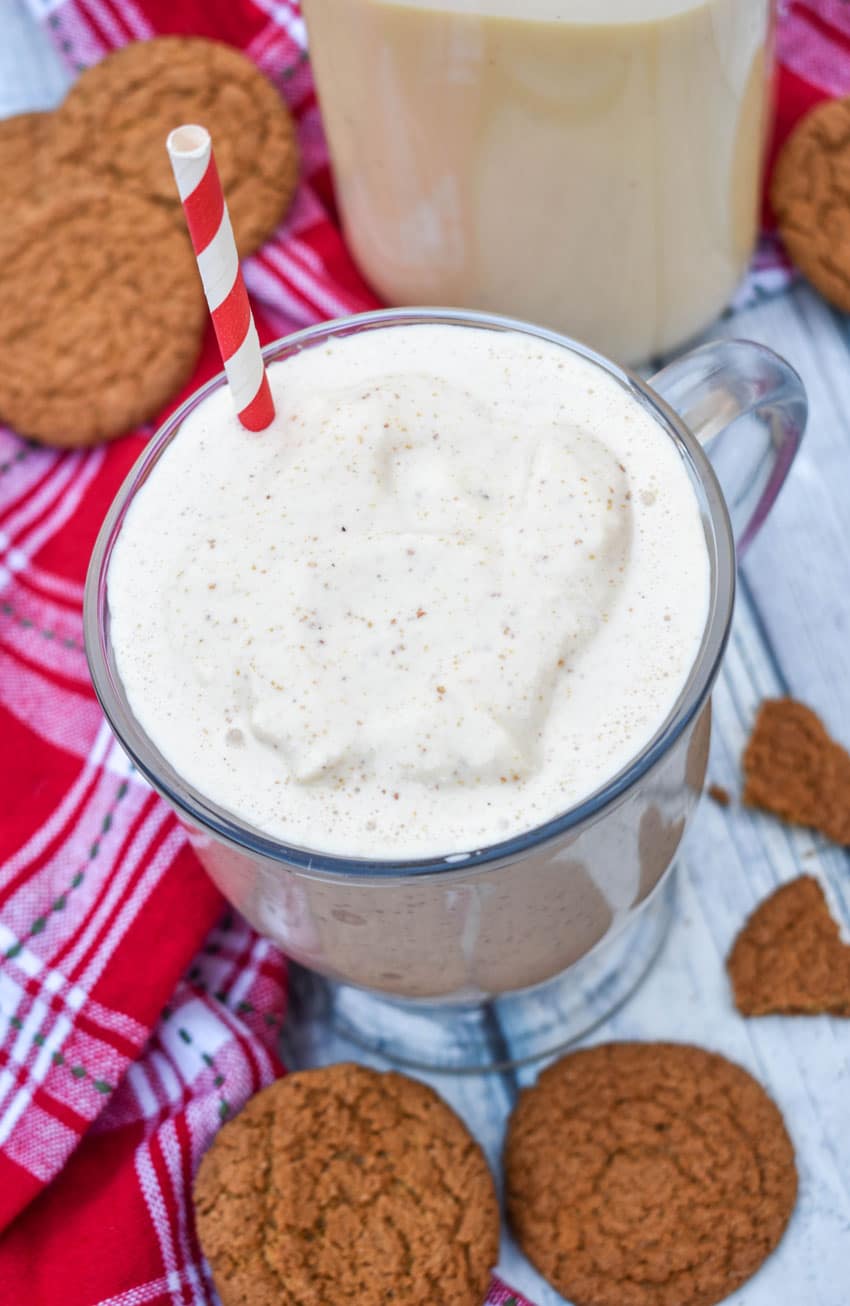 a gingerbread milkshake in a glass mug with a red and whipped striped straw sticking out