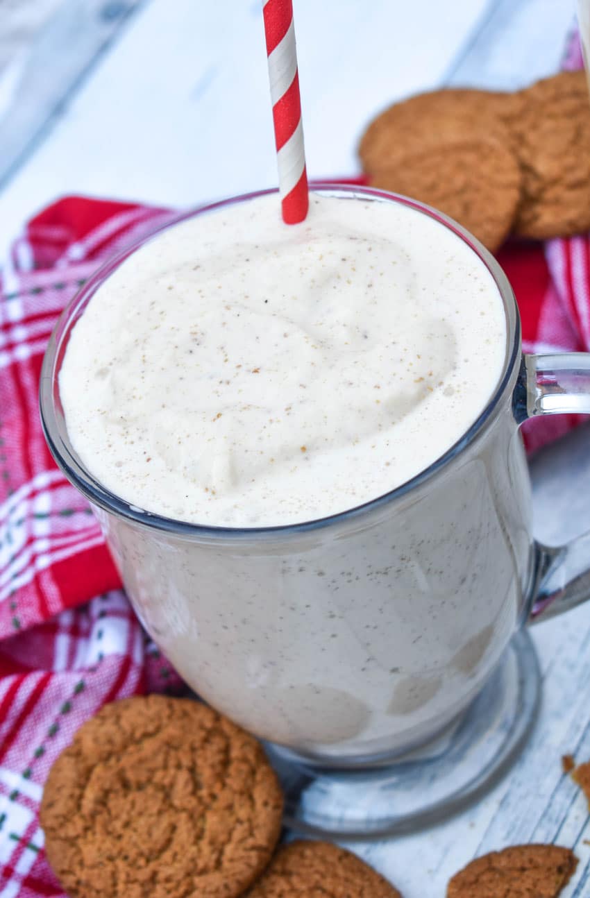 a gingerbread milkshake in a glass mug with a red and whipped striped straw sticking out