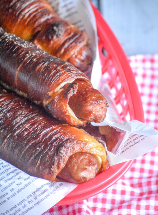 THREE EASY HOMEMADE PRETZEL DOGS IN A PAPER LINED RED FOOD BASKET