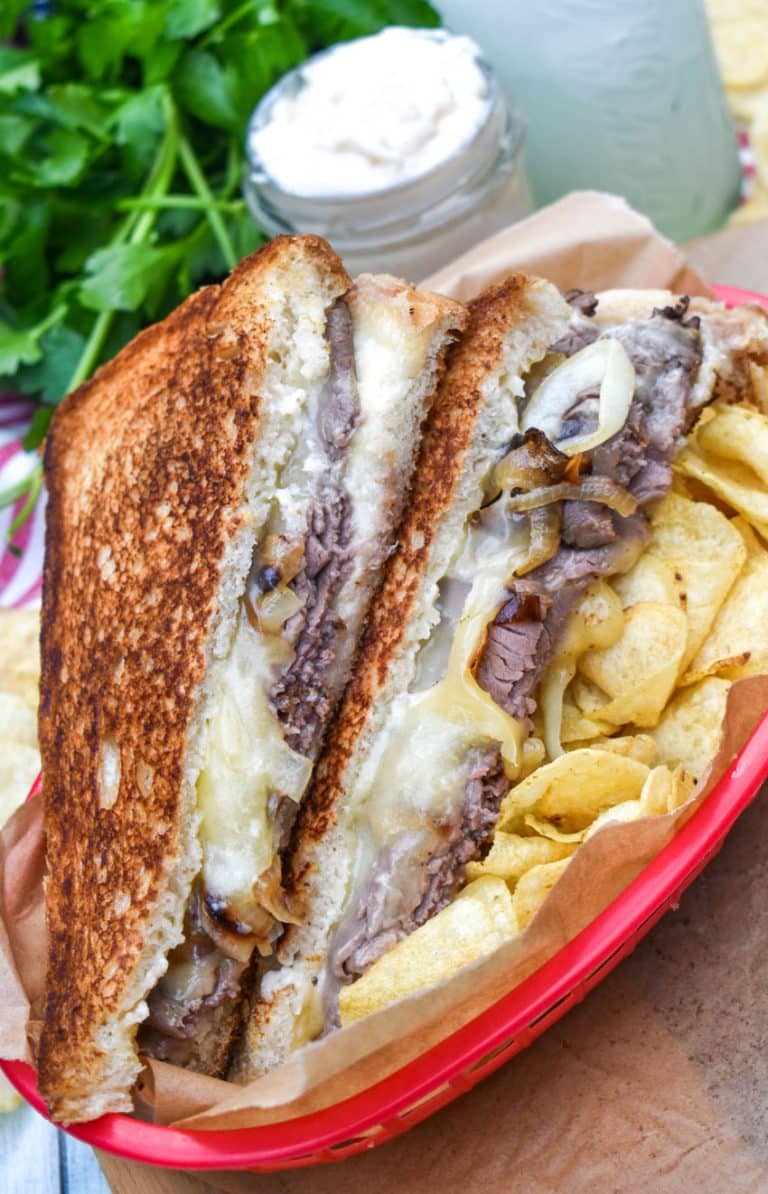 two halves of roast beef grilled cheese with smoked gouda on a bed of potato chips in a red plastic food basket