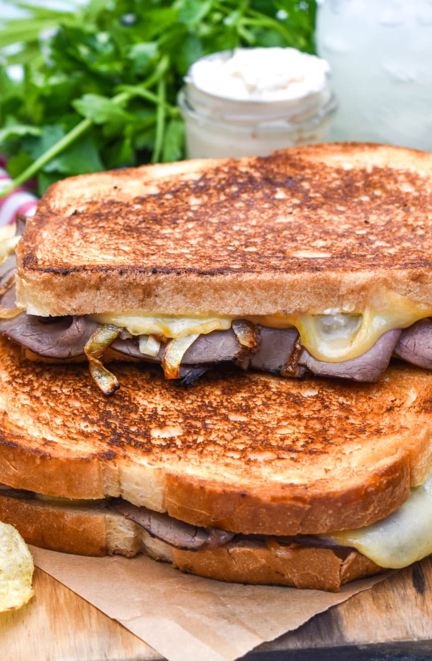 two roast beef grilled cheese sandwiches with smoked gouda stacked together on a wooden cutting board