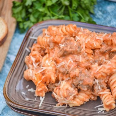 two timin pasta served on a square brown plate with fresh herbs and bread in the background