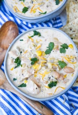 creamy white chicken chili in two gray bowls topped with shredded cheese and fresh cilantro