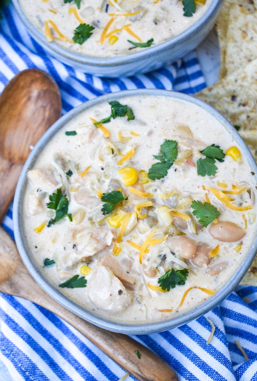 creamy white chicken chili in two gray bowls topped with shredded cheese and fresh cilantro