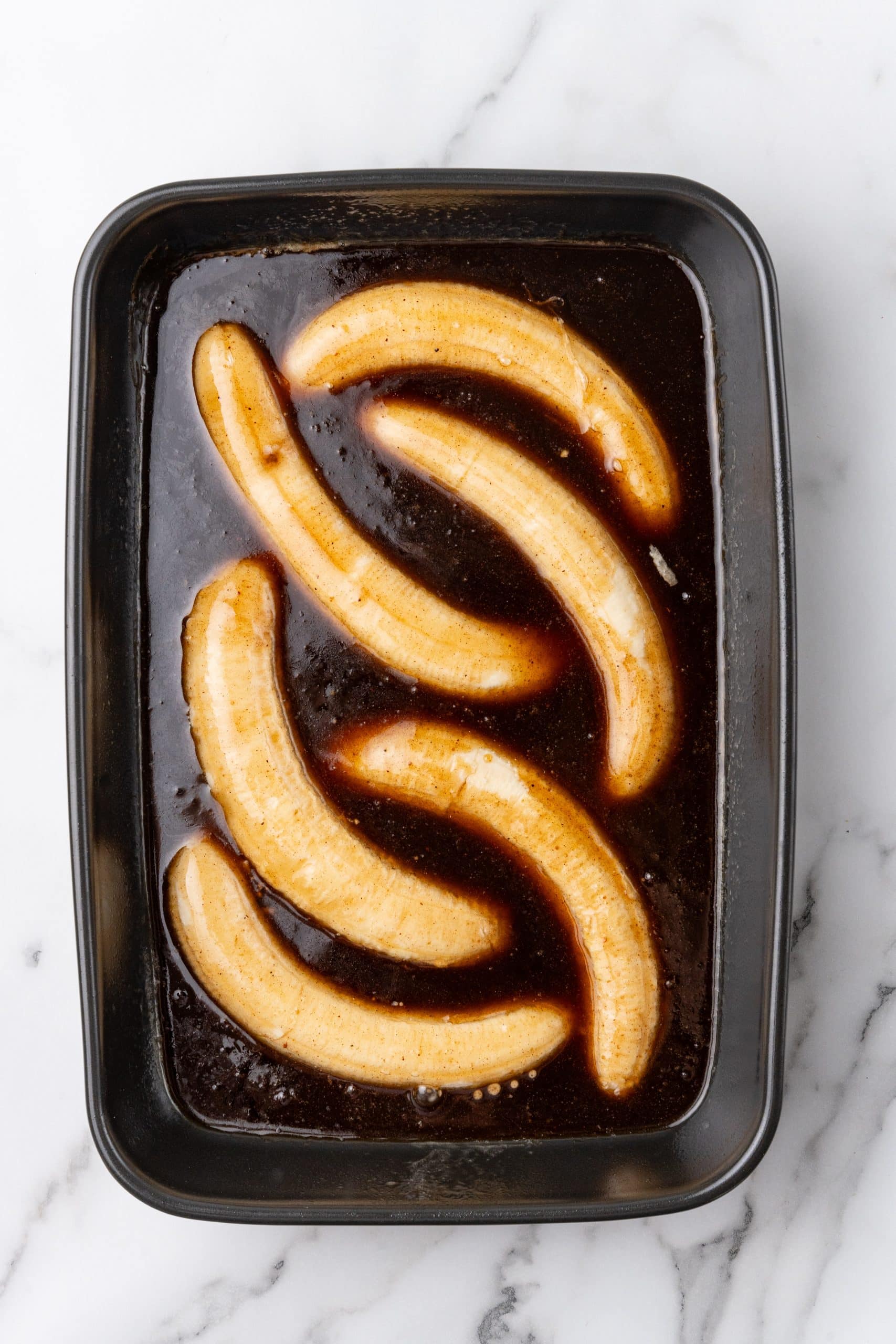 bananas foster rum sauce poured over bananas in a metal brownie pan