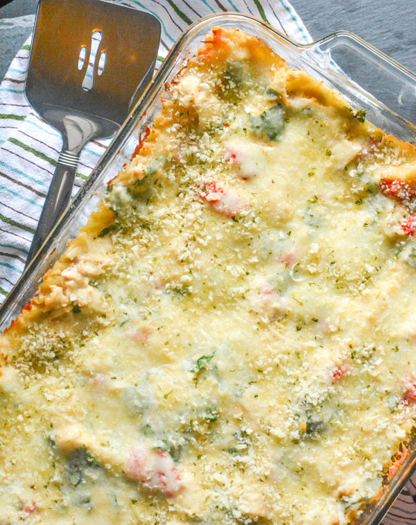 a Chicken Caesar Lasagna shown baked in a glass 9x13 baking dish with a spatula on the side for serving