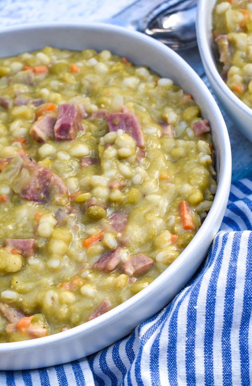 SLOW COOKER SPLIT PEA SOUP WITH HAM IN A WHITE SOUP BOWL WITH SLICES OF FRESH BREAD ON THE SIDE