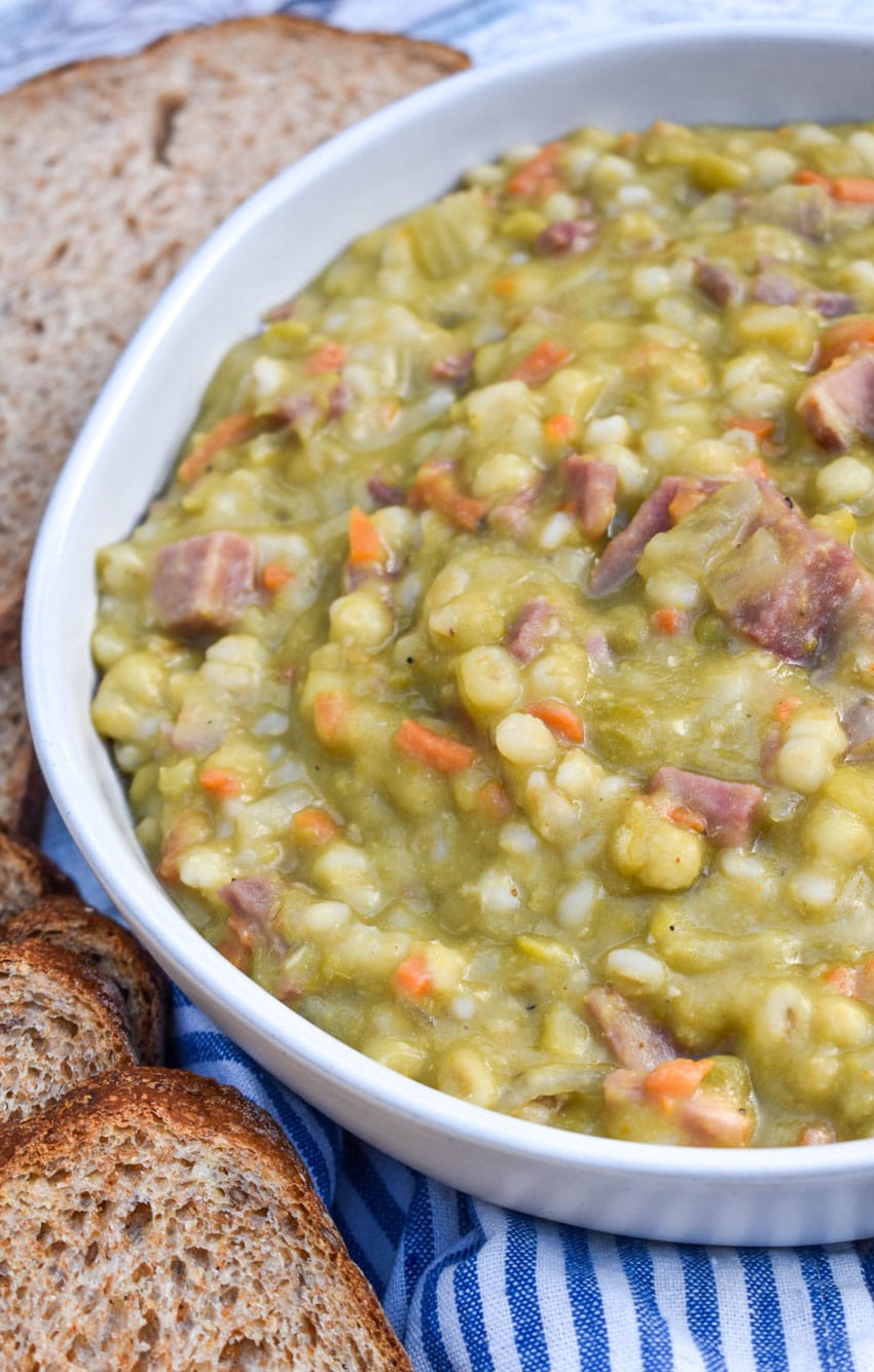 SLOW COOKER SPLIT PEA SOUP WITH HAM IN A WHITE SOUP BOWL WITH SLICES OF FRESH BREAD ON THE SIDE