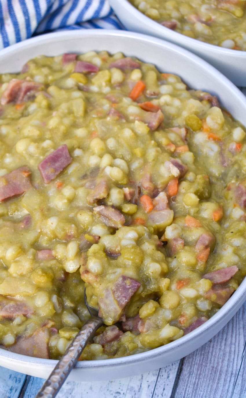 SLOW COOKER SPLIT PEA SOUP WITH HAM IN A WHITE SOUP BOWL WITH SLICES OF FRESH BREAD ON THE SIDE