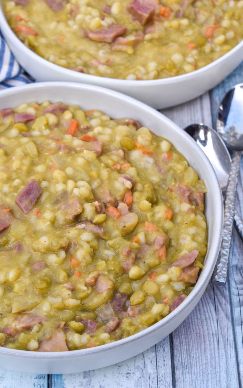 SLOW COOKER SPLIT PEA SOUP WITH HAM IN A WHITE SOUP BOWL WITH SLICES OF FRESH BREAD ON THE SIDE