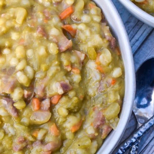 SLOW COOKER SPLIT PEA SOUP WITH HAM IN A WHITE SOUP BOWL WITH SLICES OF FRESH BREAD ON THE SIDE