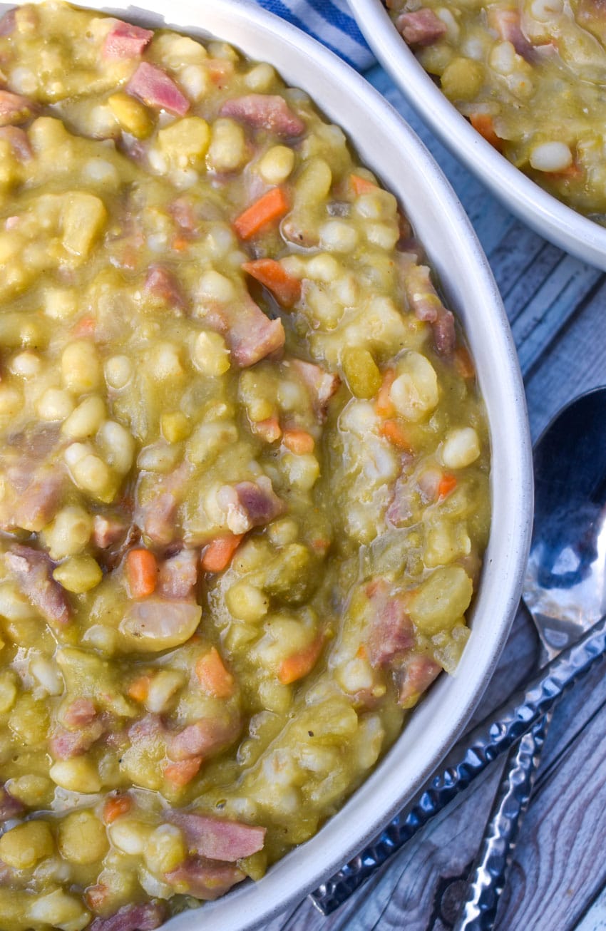 SLOW COOKER SPLIT PEA SOUP WITH HAM IN A WHITE SOUP BOWL WITH SLICES OF FRESH BREAD ON THE SIDE