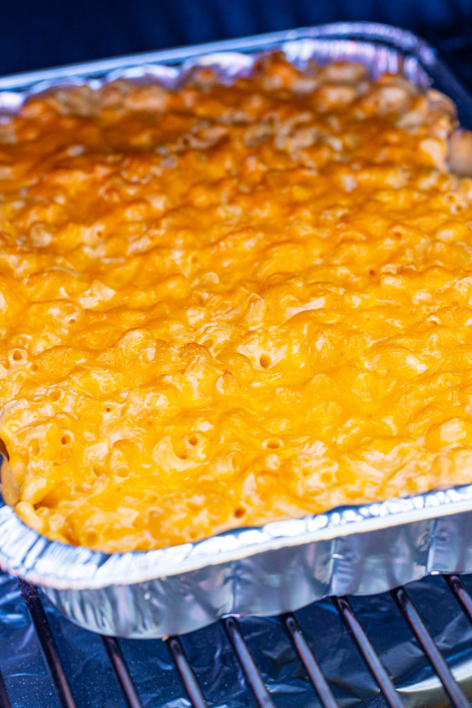 an aluminum pan filled with smoked macaroni and cheese shown on a rack in a smoker