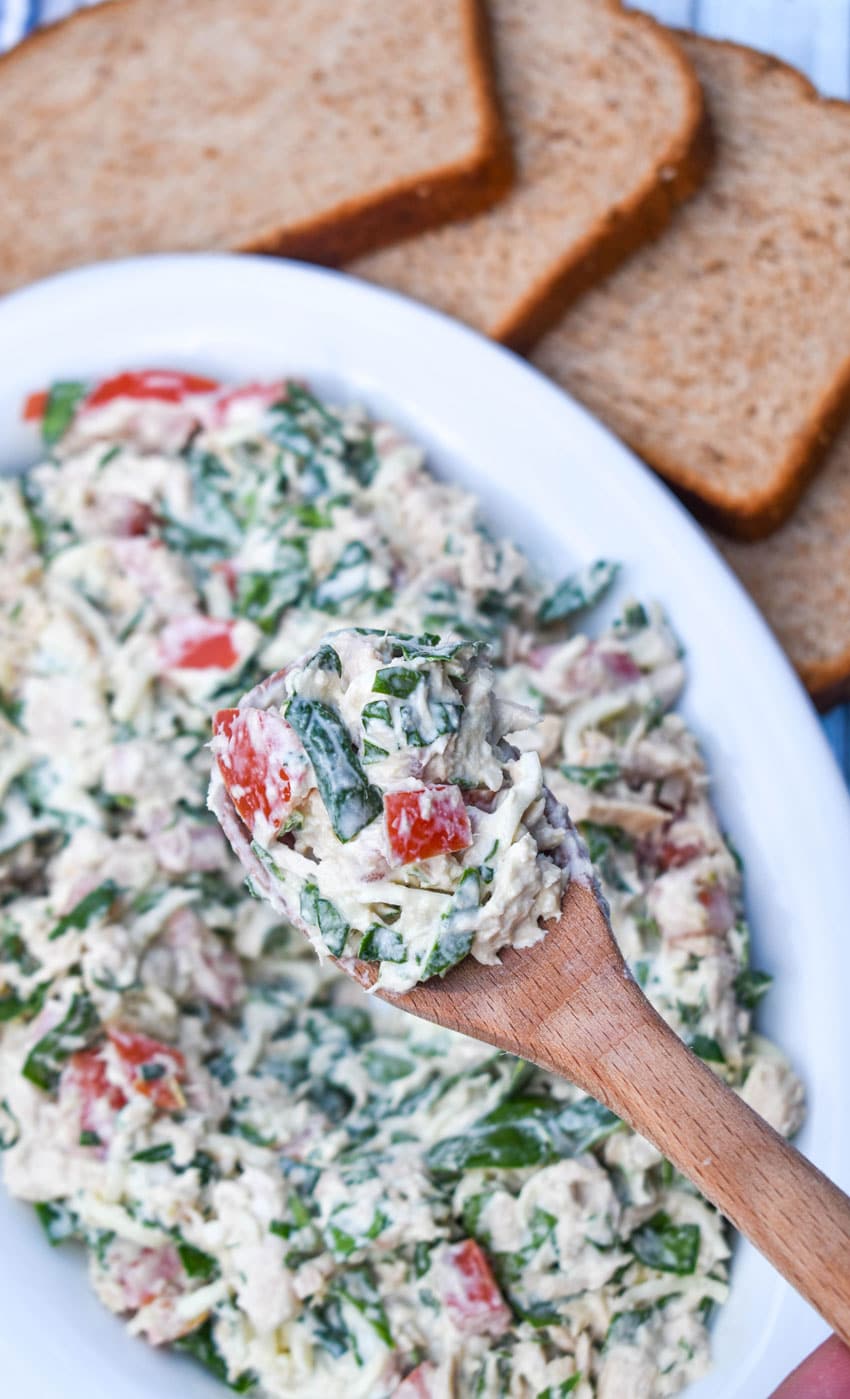 a wooden spoon holding up a scoop of spinach and tomato tuna salad with greek yogurt