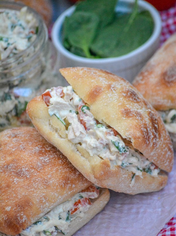 tuna salad sandwiches on ciabatta bread next to a bowl of fresh baby spinach