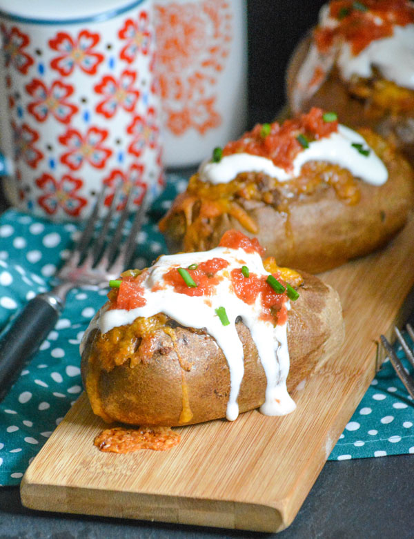 twice baked tex mex stuffed potatoes arranged in a line on a narrow wooden cutting board