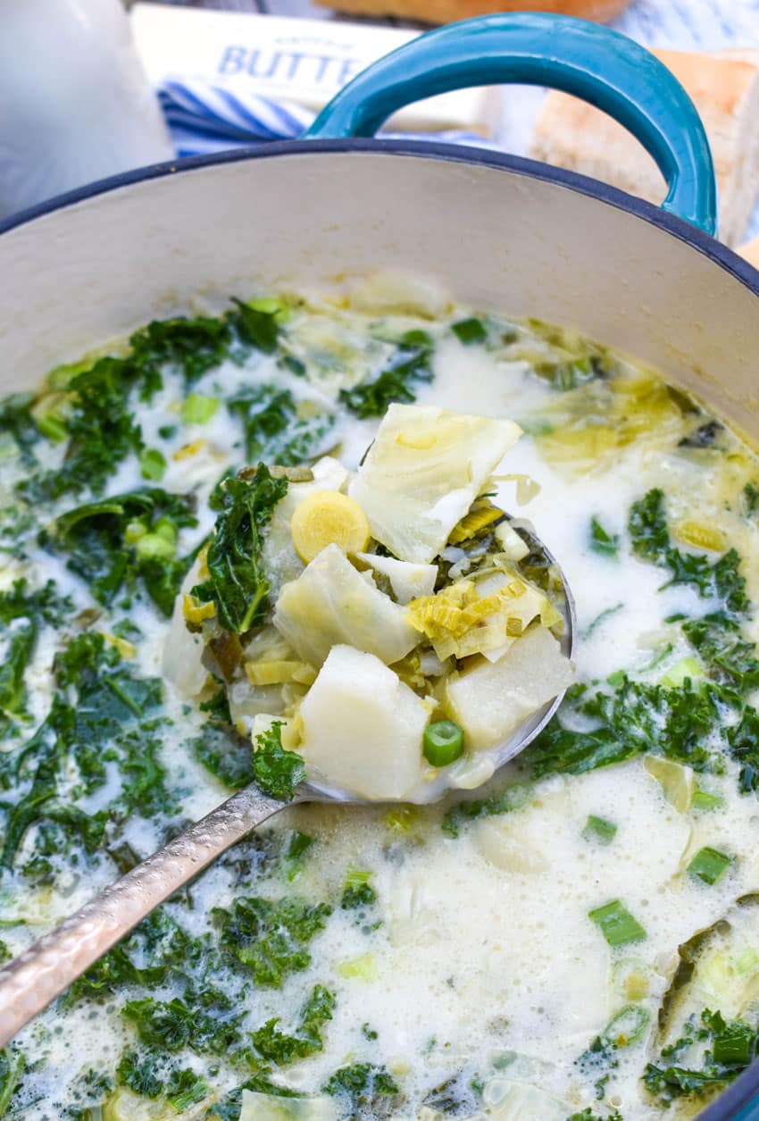 a silver ladle scooping colcannon potato soup out of a large blue dutch oven