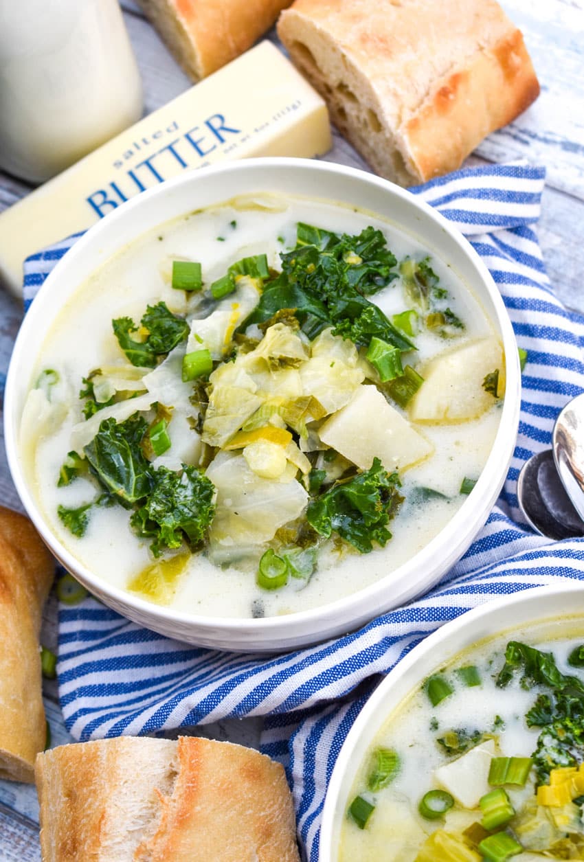 colcannon potato soup in two white bowls with slices of fresh baguette on the sides