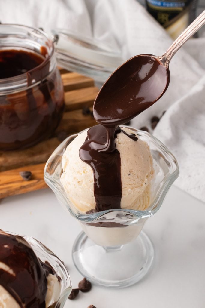 bailey's Irish cream chocolate sauce being spooned over a scoop of ice cream in a glass bowl