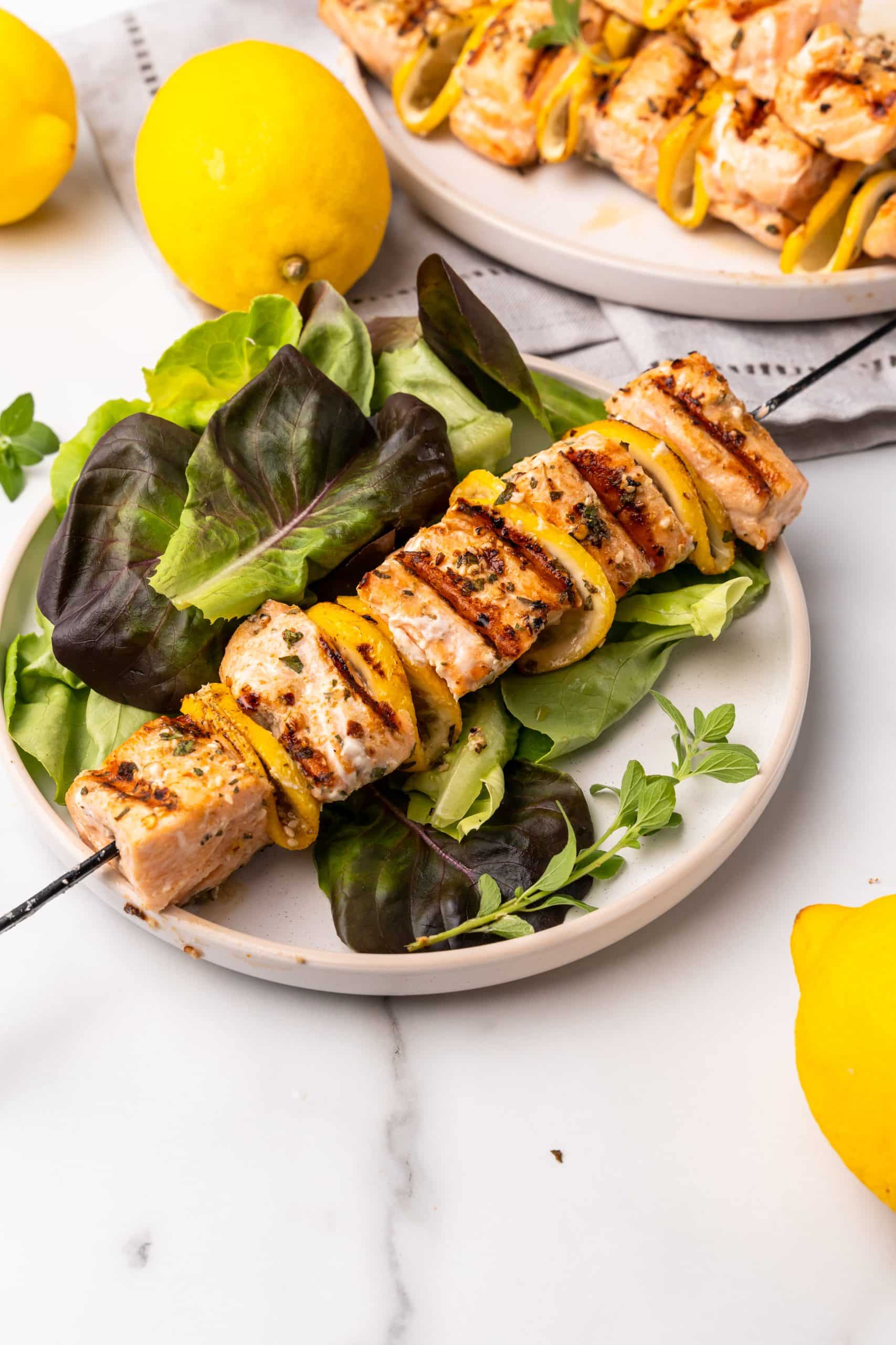a grilled salmon kebabs on a bed of lettuce on a white plate