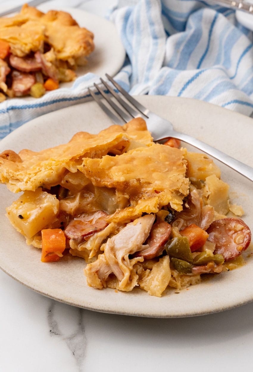 a slice of smoked sausage and chicken pot pie on a small white plate