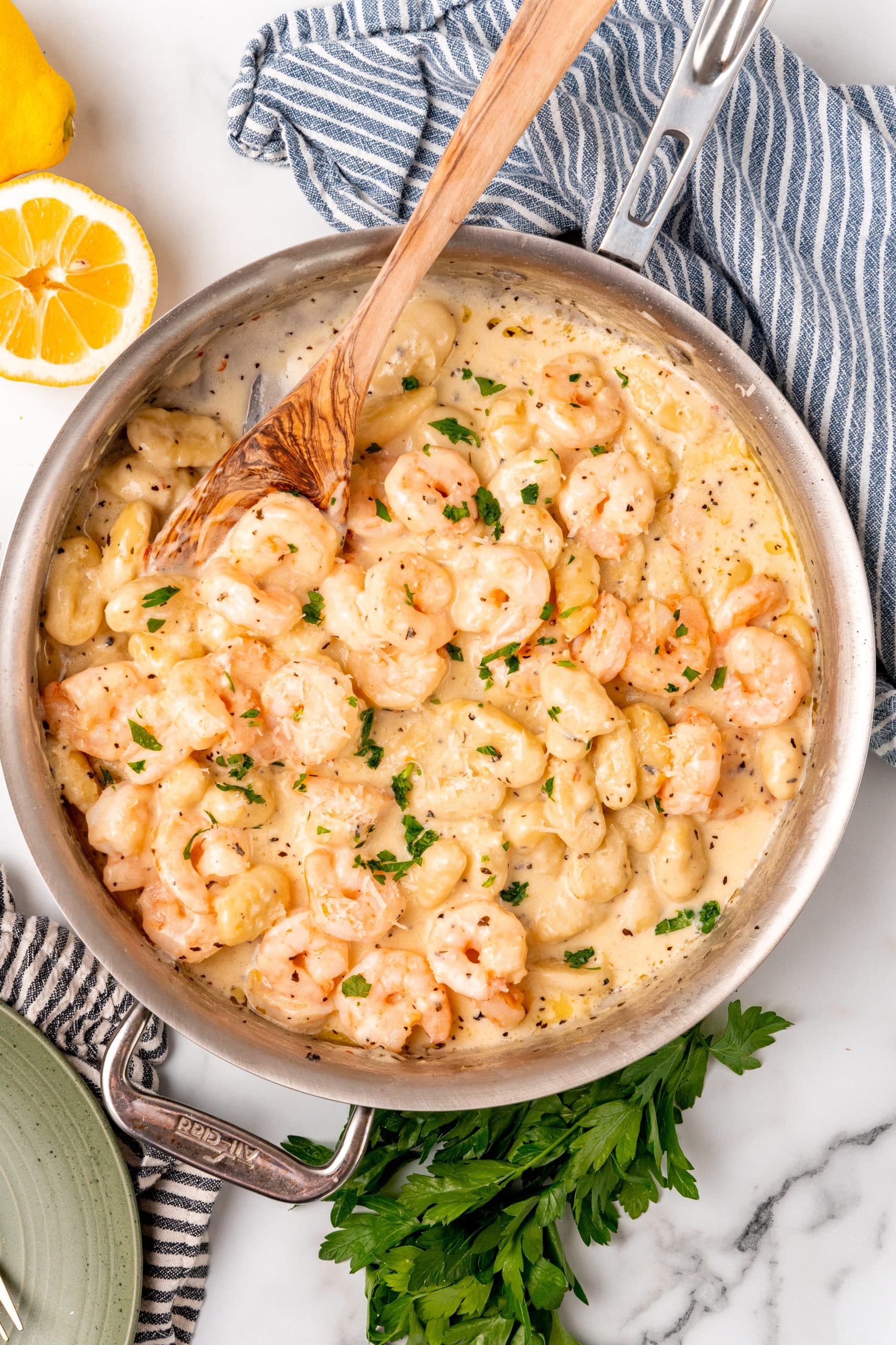 a wooden spoon resting in a silver skillet filled with creamy gnocchi shrimp scampi
