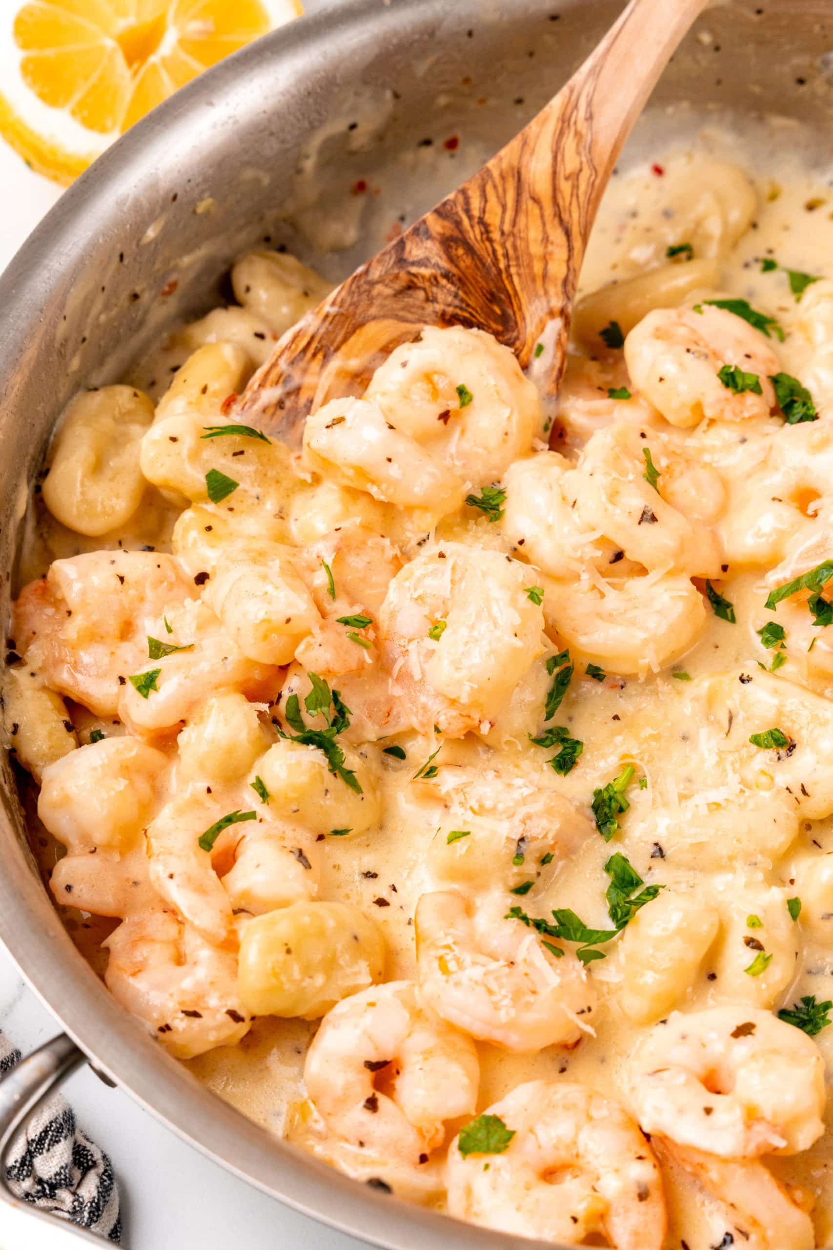 a wooden spoon resting in a silver skillet filled with creamy gnocchi shrimp scampi